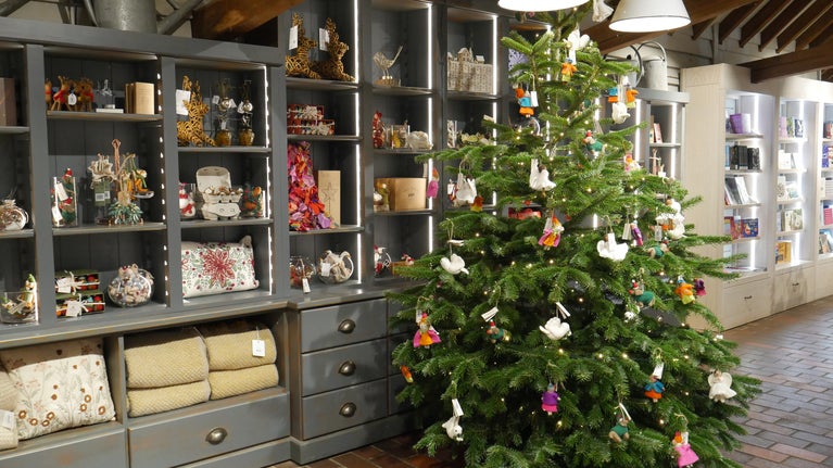 A Christmas tree stands in the middle of a shop floor, decorated with felt animals, with filled shelves behind it
